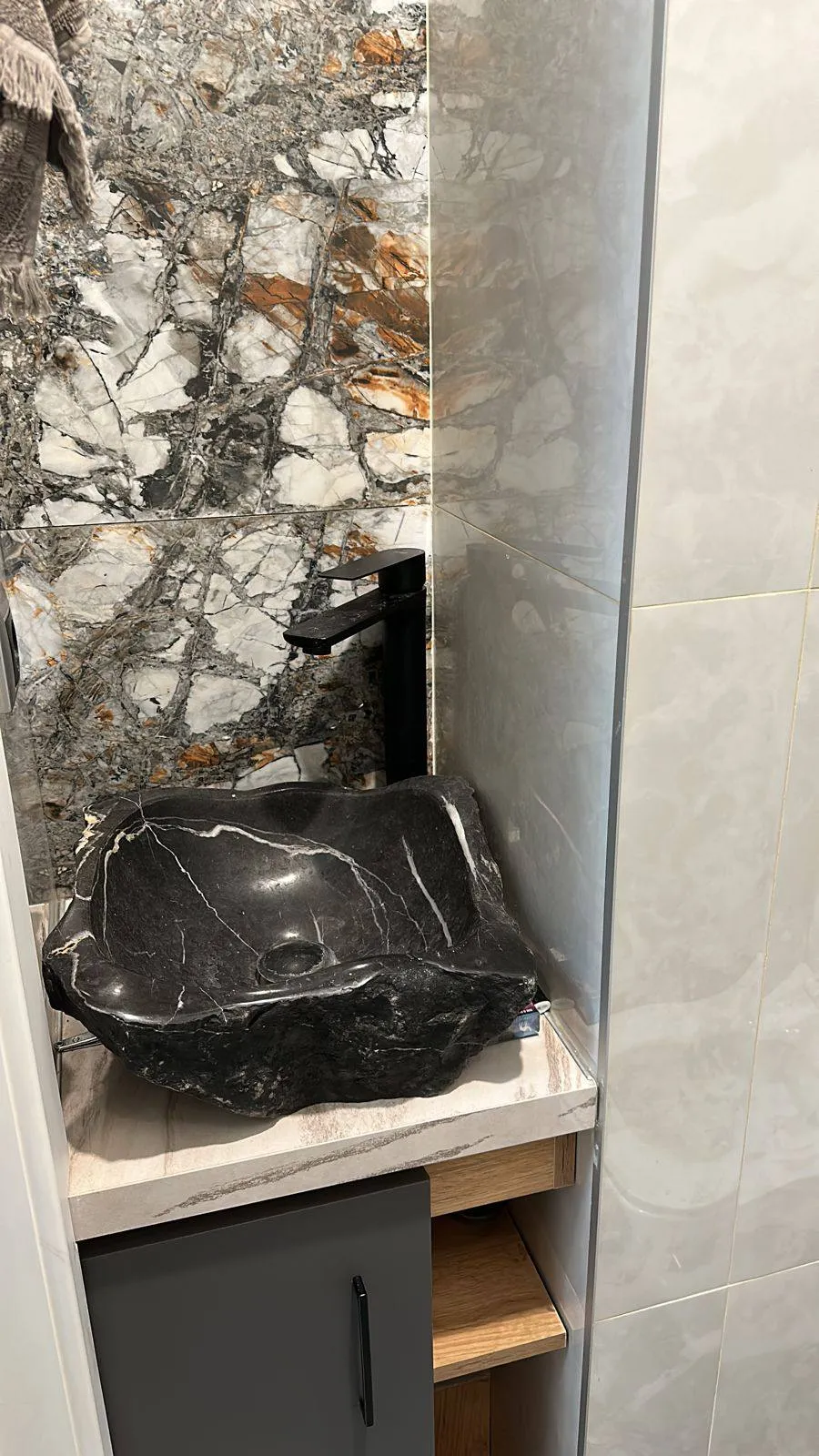 Раковина из чёрного камня на светлой столешнице, стена из камня с рыжими прожилками